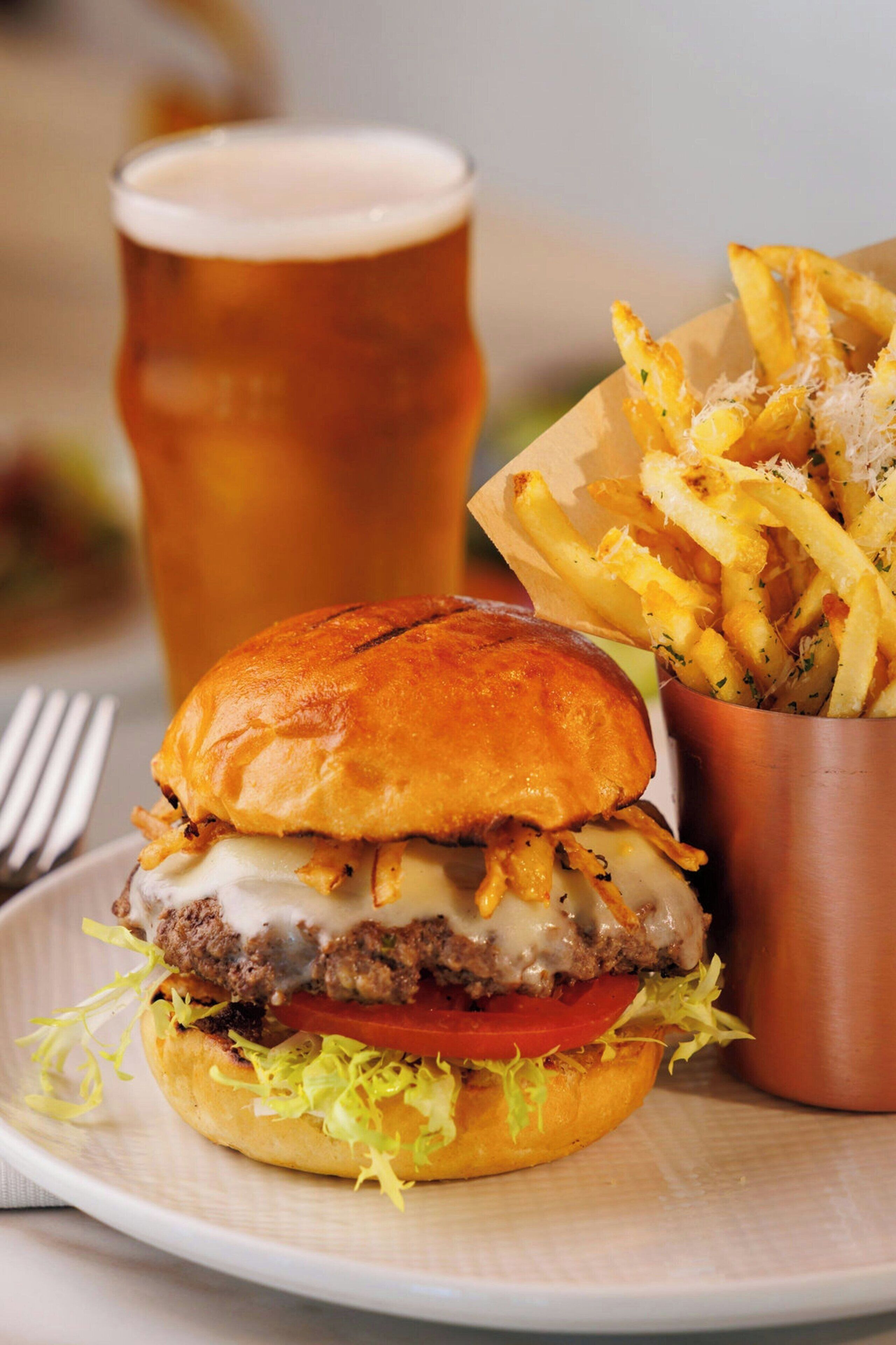 Un hamburger accompagné de frites et d’un verre de bière, le tout servi sur une assiette.
