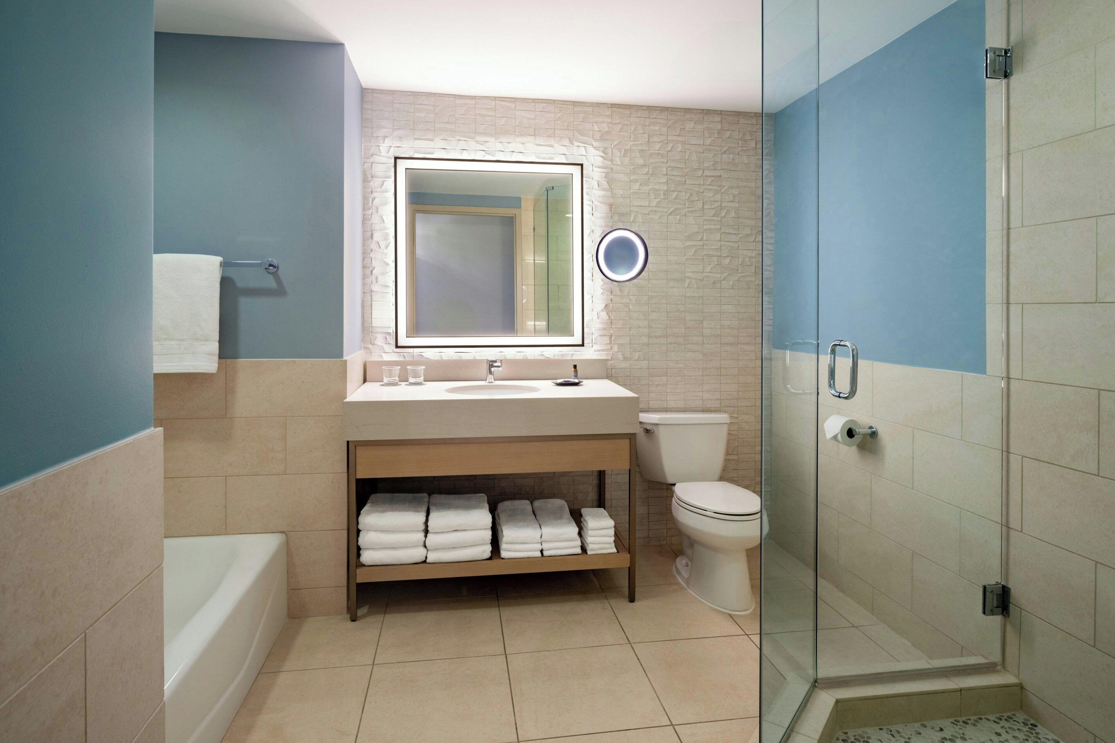 A modern bathroom with a bathtub, a sink with a mirror, a toilet, and a glass-enclosed shower.