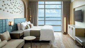A hotel room with a large bed, a sofa, a TV, and a view of the water.