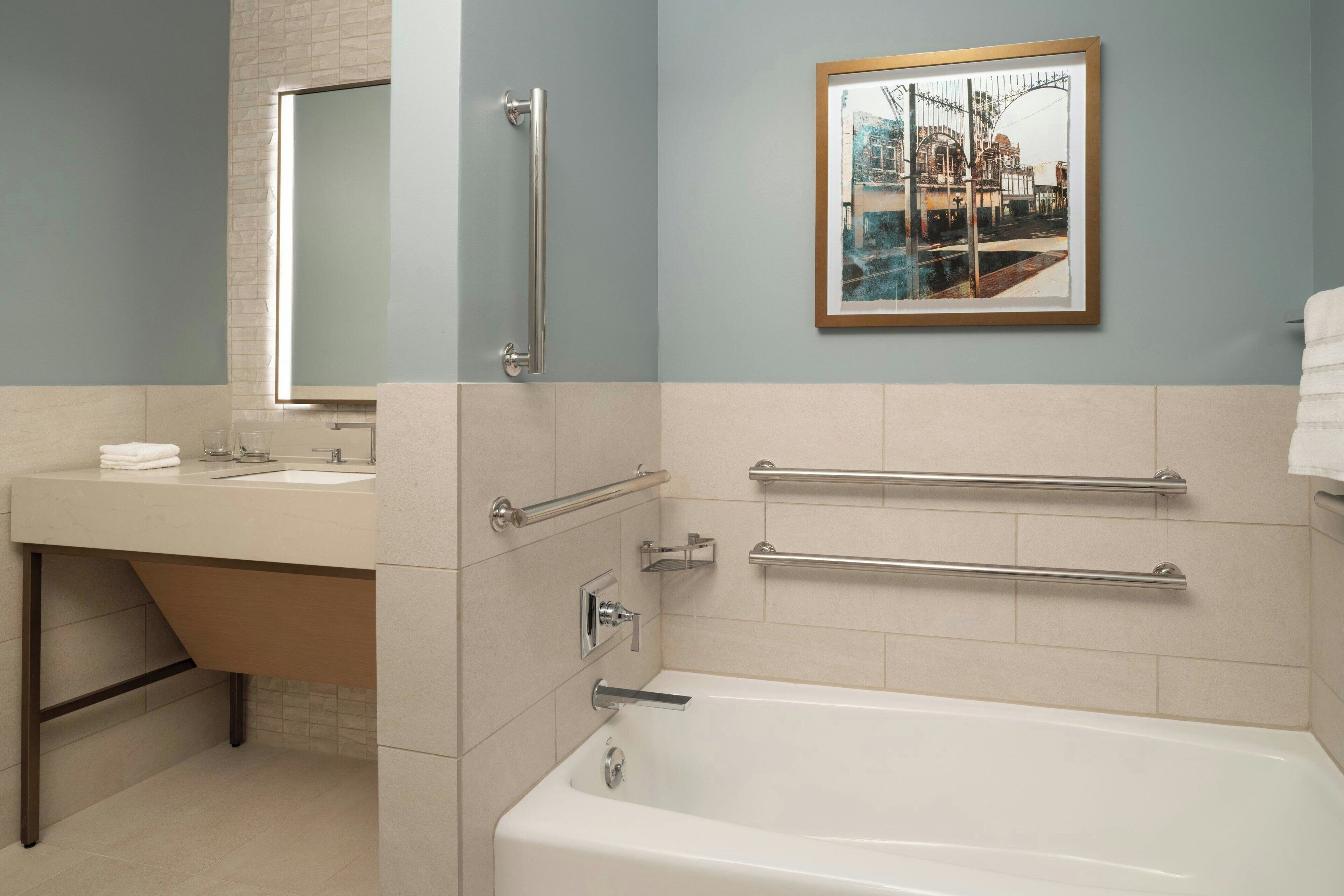 Une salle de bain moderne équipée d’une baignoire, d’un lavabo et d’un miroir. Des barres d’appui ont été installées pour plus de sécurité.