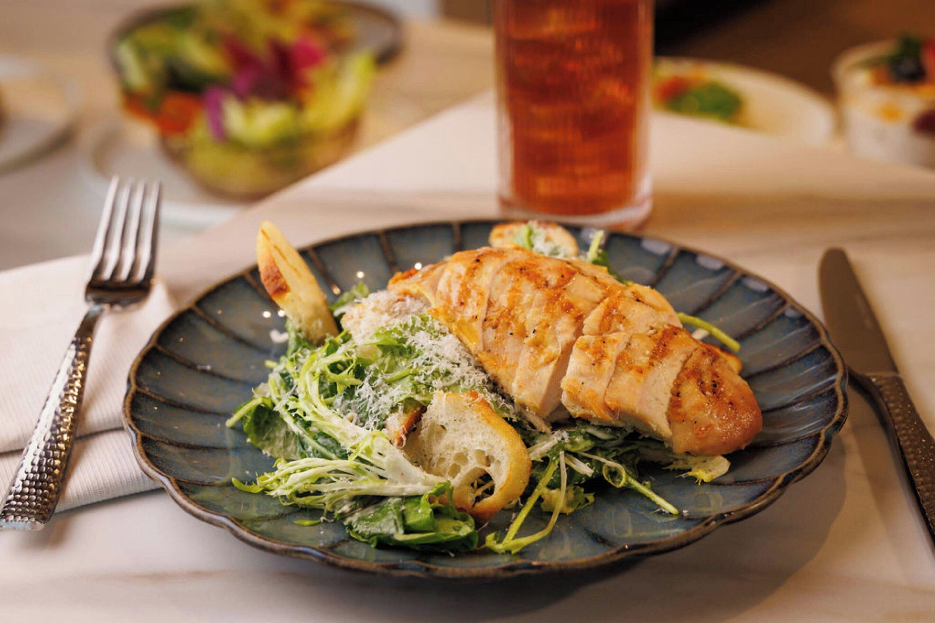 A plate with a grilled chicken breast, greens, and bread on a ceramic plate.