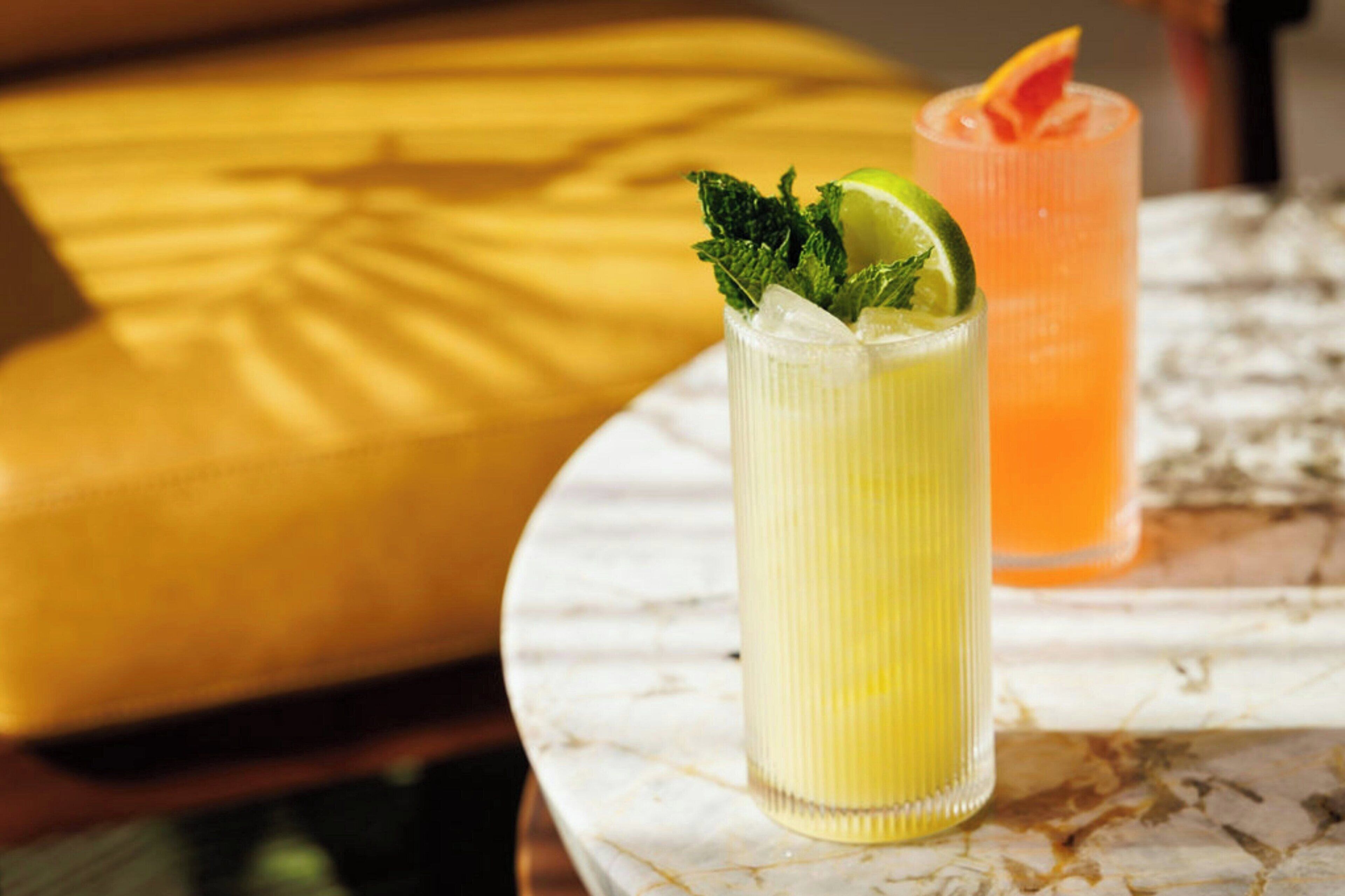 Two tall glasses of beverages on a marble table with a yellow cushion in the background.