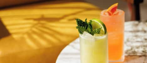 Two tall glasses of beverages on a marble table with a yellow cushion in the background.