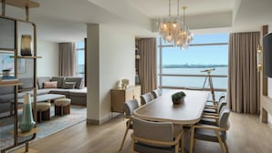 A modern living room with a large dining table, comfortable seating, a bookshelf, and a view of the water.