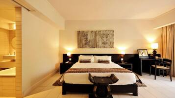 A hotel room with a large bed, bedside tables, a desk, a chair, and artwork on the wall.