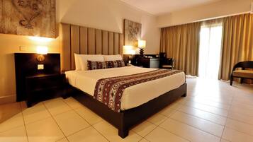 A hotel room with a large bed, two bedside tables with lamps, a desk with a chair, and a large window with curtains.