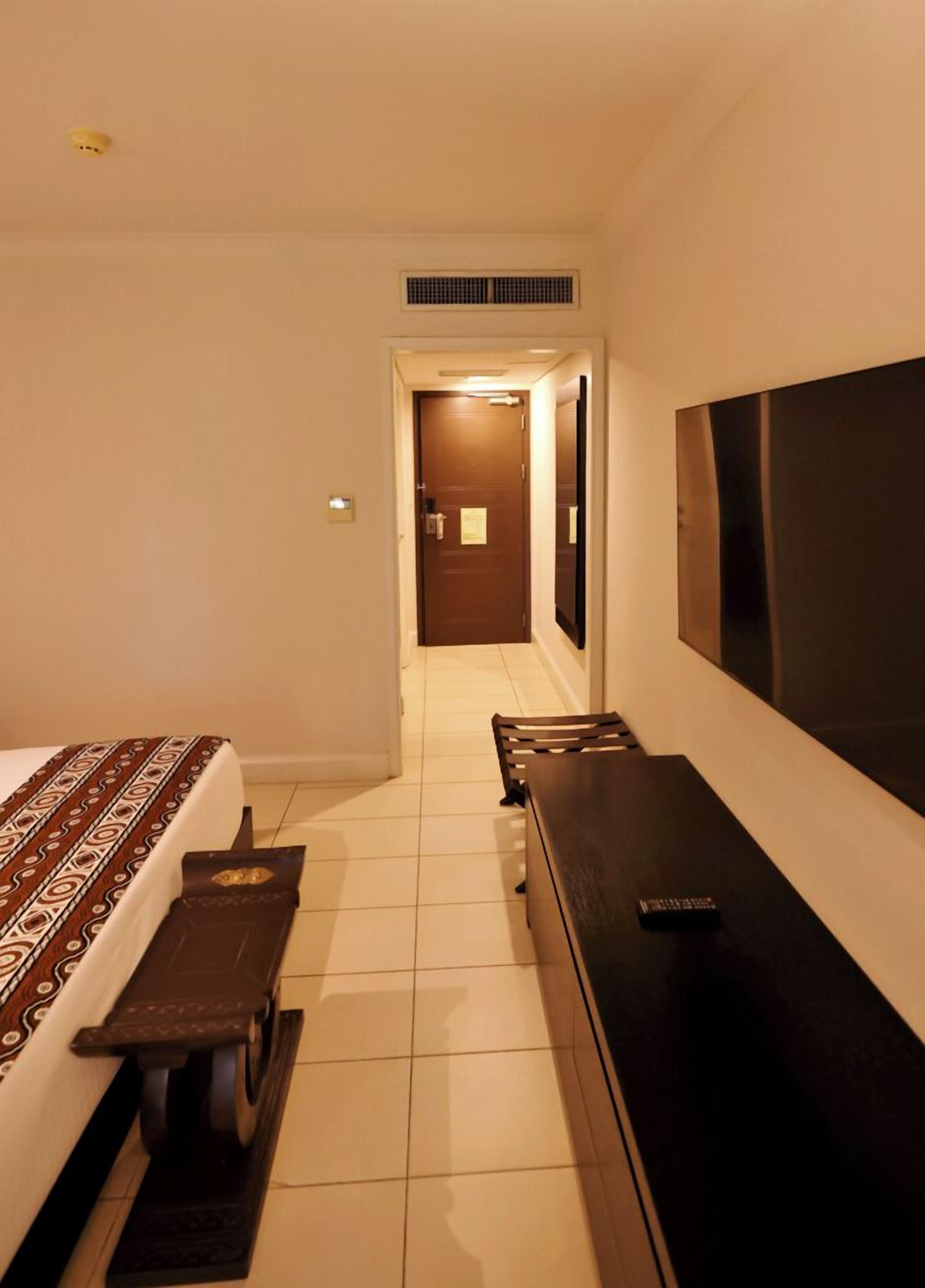 Una habitación de hotel con cama, escritorio, silla, televisor y puerta que da a un pasillo.