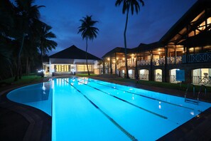 A swimming pool with a curved edge, adjacent to a building with multiple balconies and a covered area.