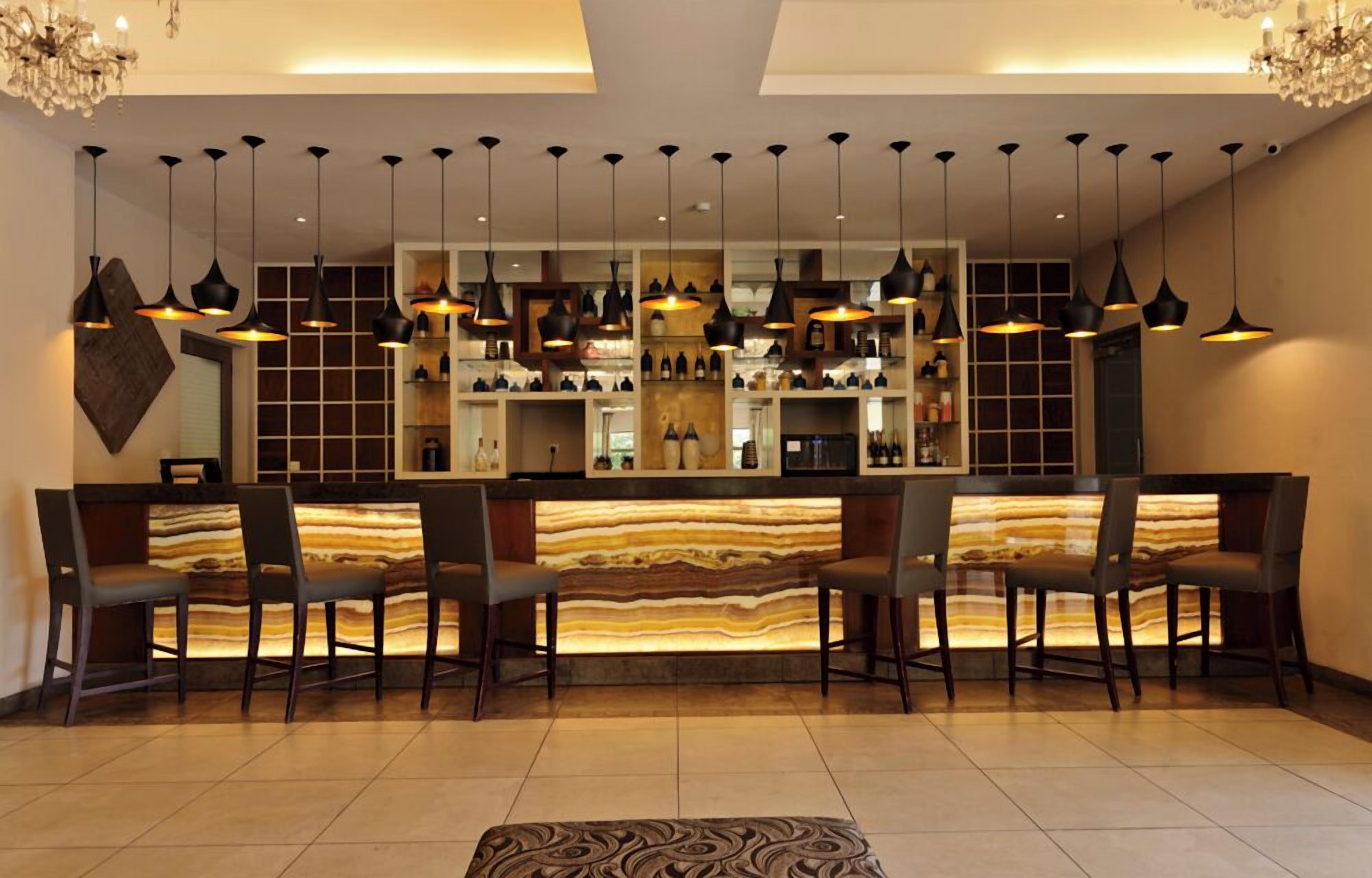 A modern bar area with a marble countertop, multiple hanging pendant lights, and a variety of bottles and glasses on shelves.