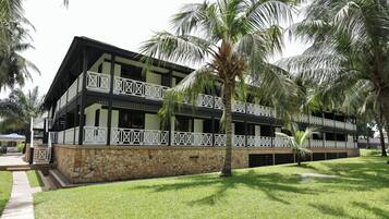 Un edificio de dos pisos con balcones, cimientos de piedra y palmeras.