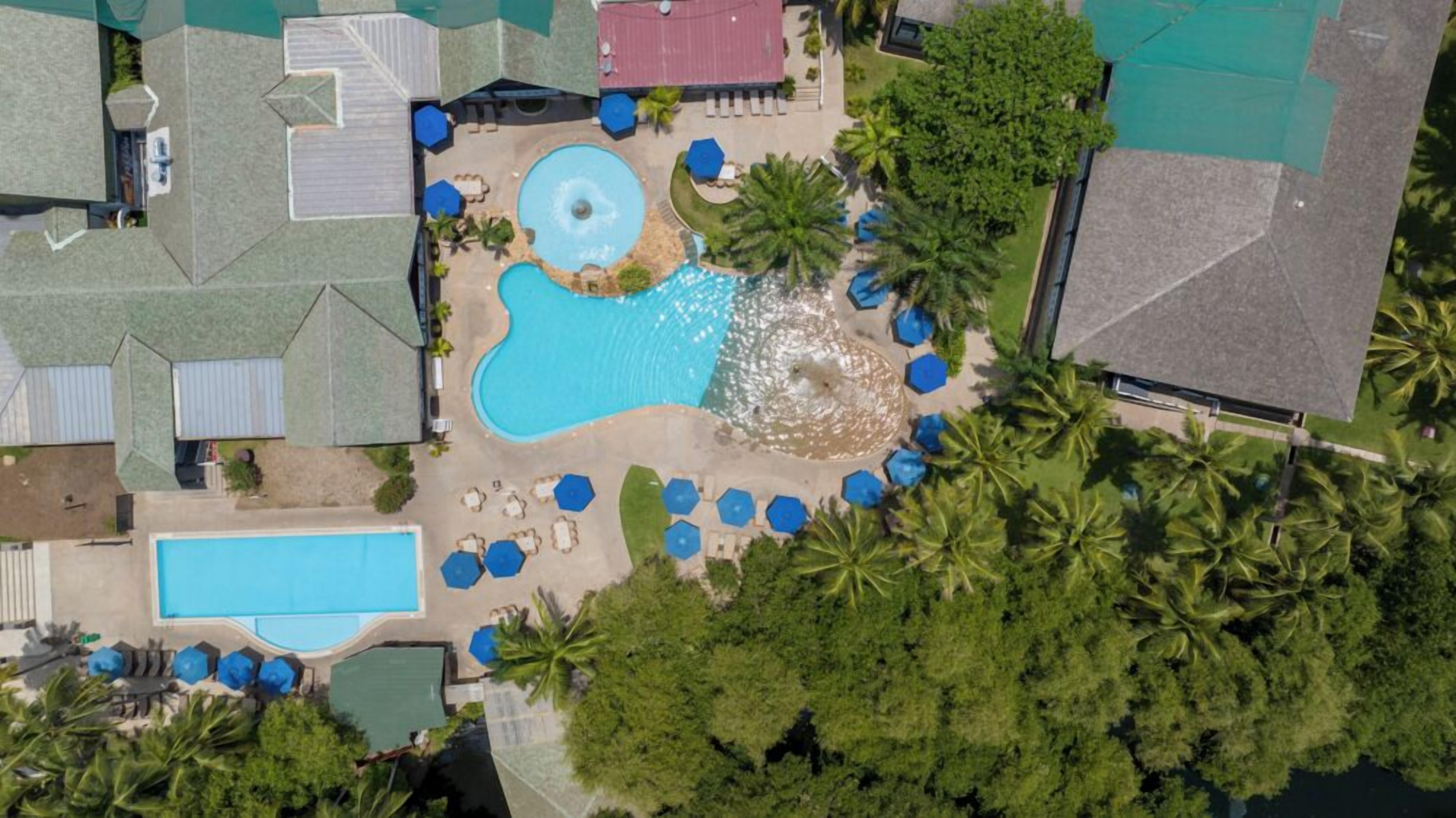 An aerial view of a resort with multiple swimming pools, lounge areas, and palm trees.