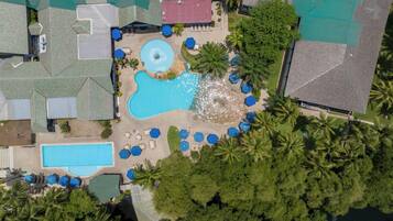 An aerial view of a resort with multiple swimming pools, lounge areas, and palm trees.