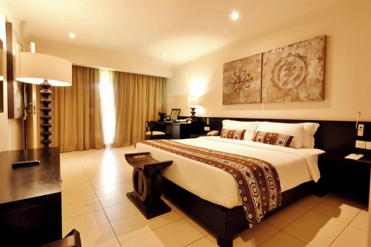 A hotel room with a large bed, a desk, a chair, a lamp, and artwork on the wall.