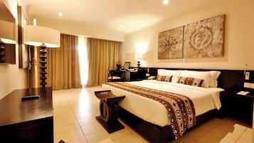 A hotel room with a large bed, a desk, a chair, a lamp, and artwork on the wall.