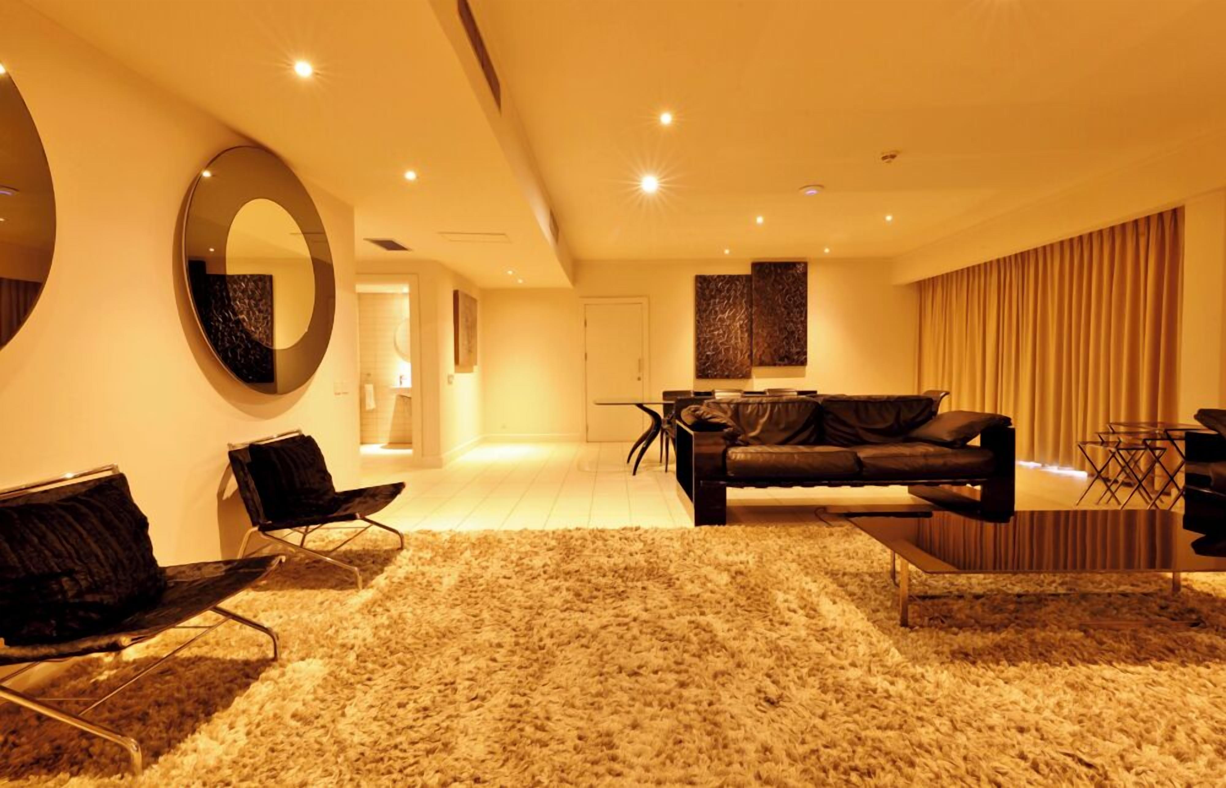 A modern living room with a sofa, two armchairs, a coffee table, and a large mirror.