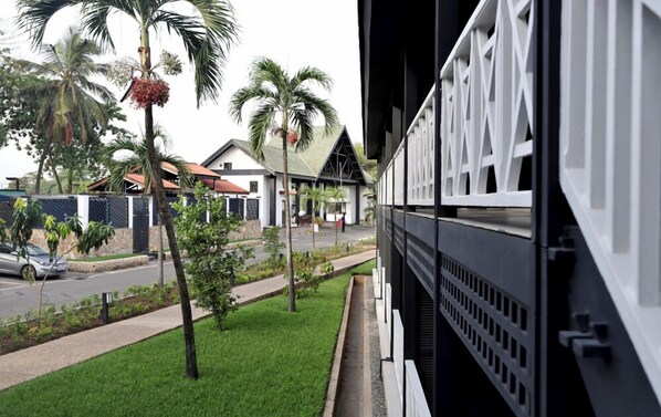 A modern building with a balcony overlooking a street lined with palm trees and a parked car.
