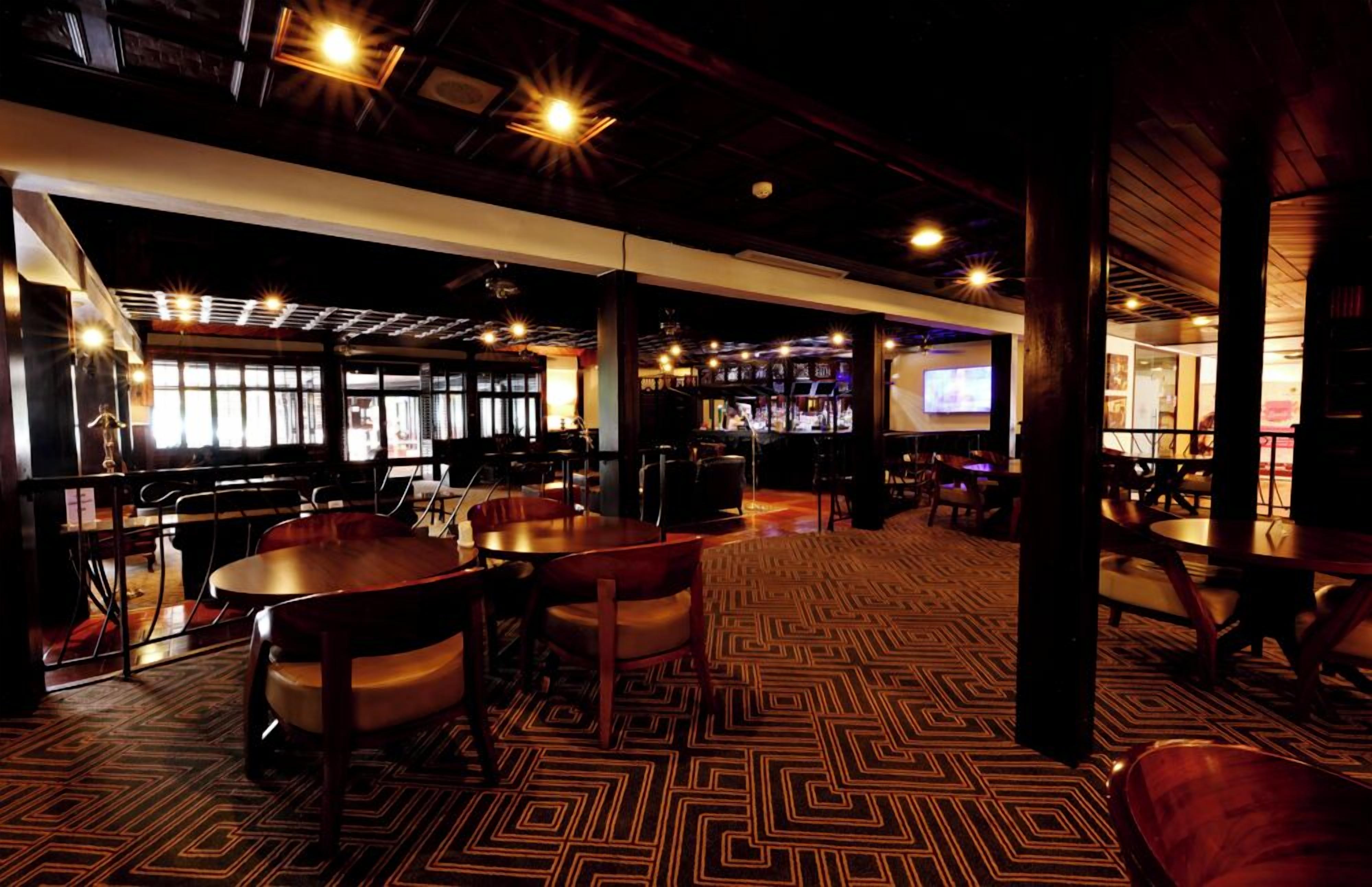 A spacious bar area with multiple seating arrangements, including round tables and chairs, and a patterned carpet.
