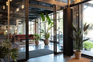 Un moderno vestíbulo de hotel con ventanas amplias, plantas en macetas y un área de descanso con un sofá rojo.