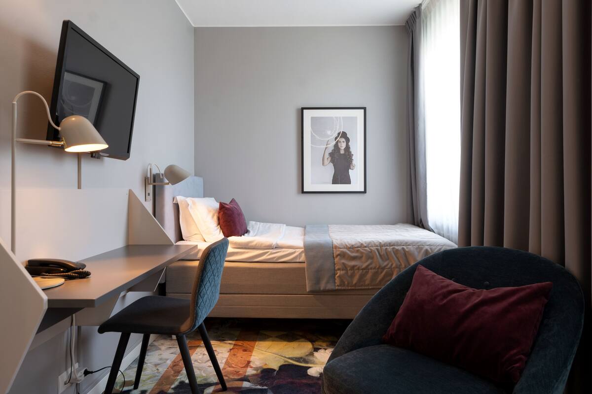 Une chambre d’hôtel comprenant un lit, un bureau avec une chaise, un téléviseur fixé au mur et un tableau encadré accroché au mur.