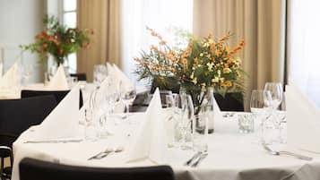 A dining table set with white tablecloths, glassware, and a centerpiece of yellow flowers and greenery.