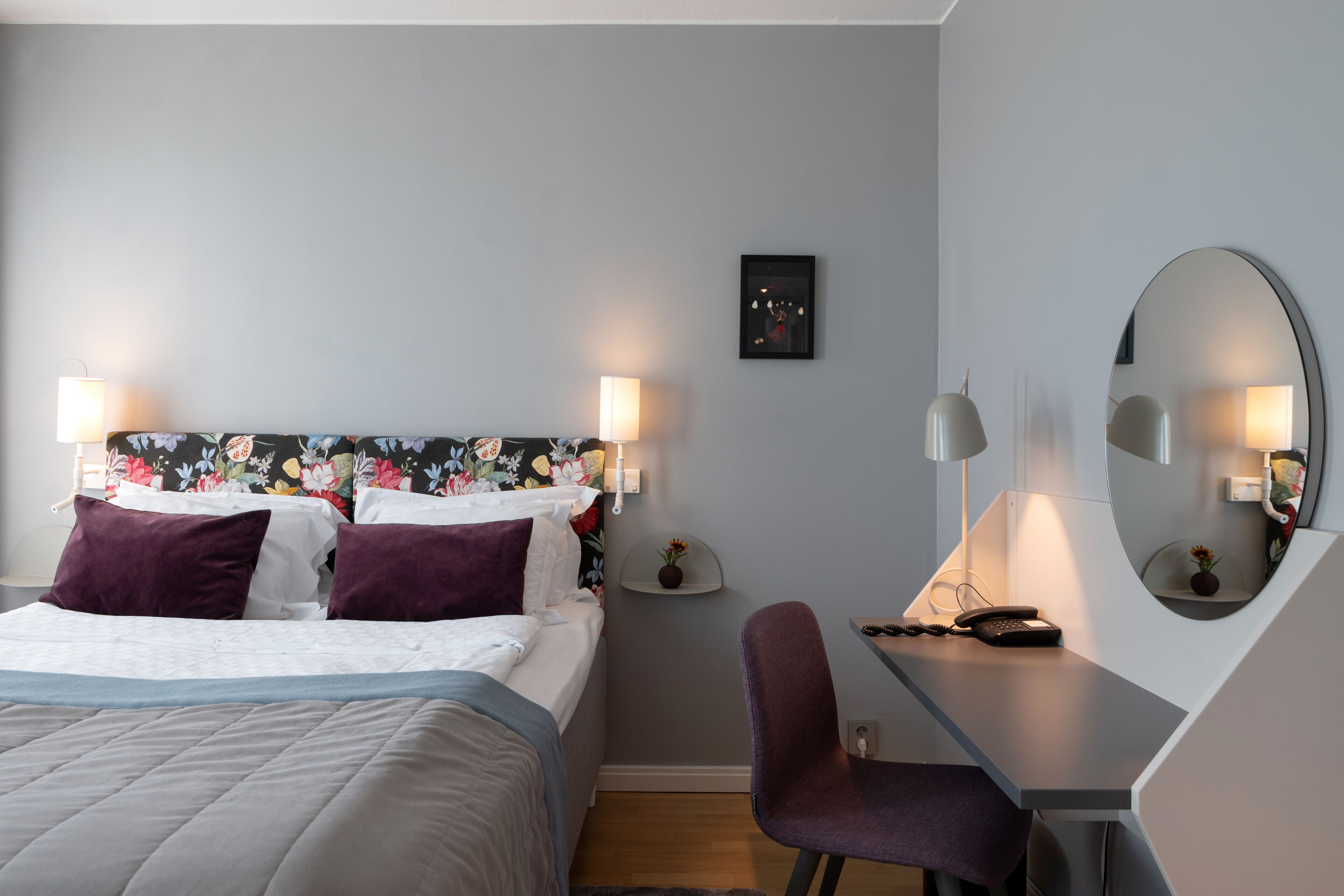 Ett modernt hotellrum med en säng, ett skrivbord, en stol och en stor spegel.