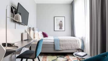 Ett modernt hotellrum med en säng, ett skrivbord, en stol och ett stort fönster med gardiner.