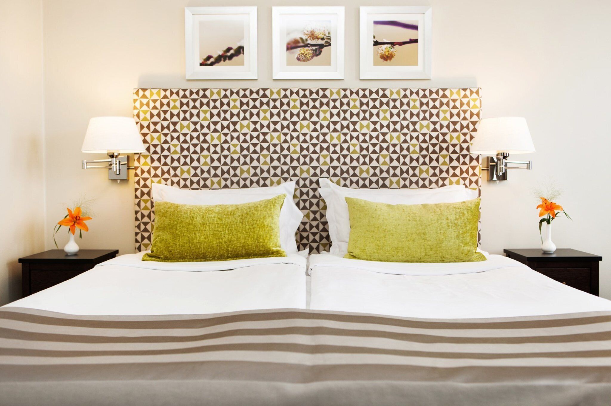 A hotel room with a patterned headboard, two bedside tables with lamps, and a bed with striped bedding.