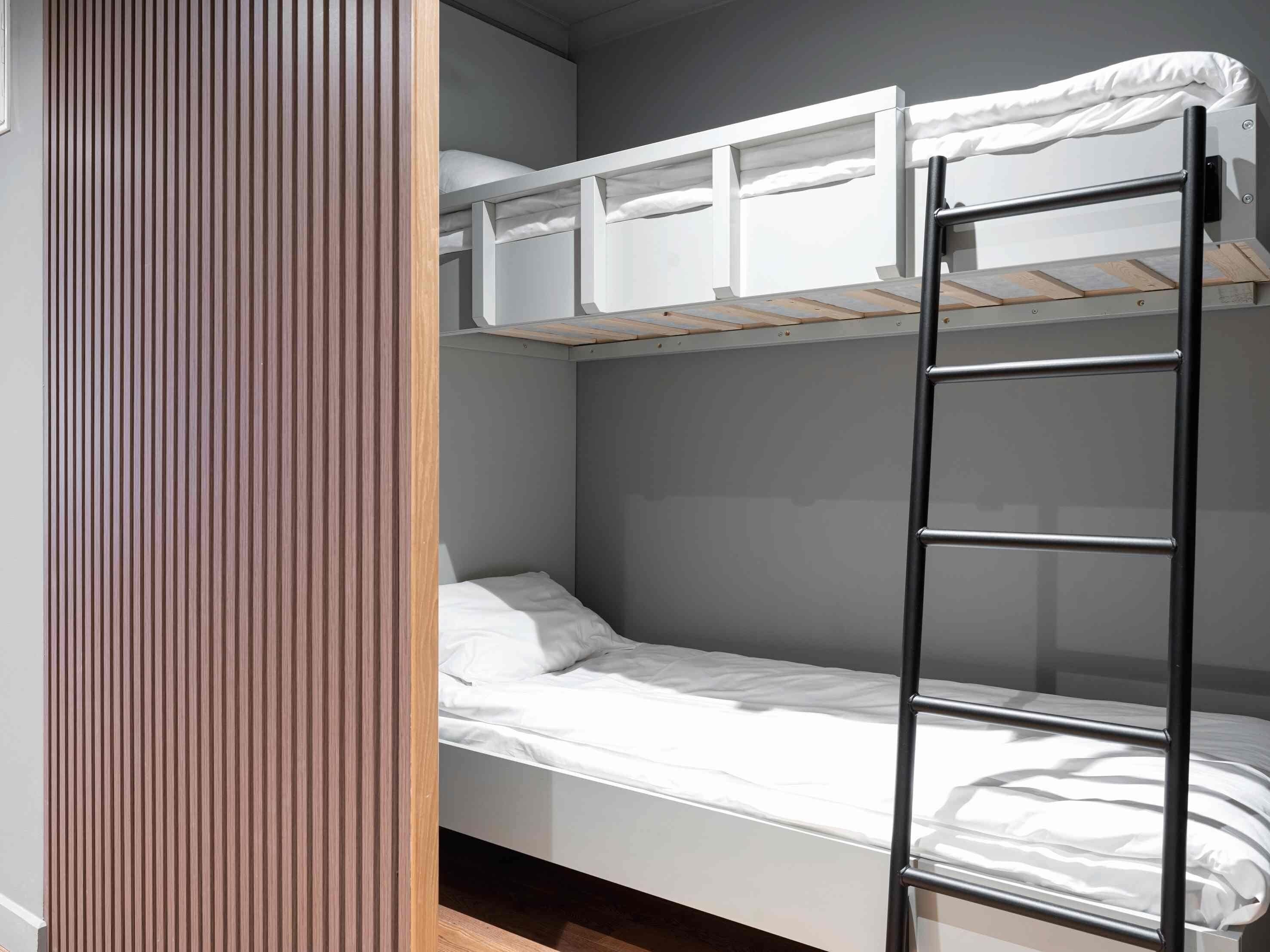 A bunk bed with a ladder, a wooden slat wall, and a grey wall.