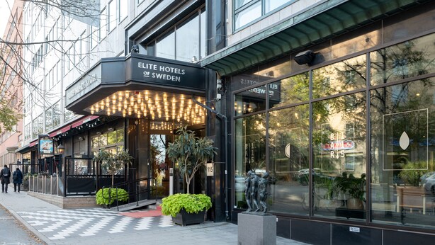 The exterior of the Elite Hotels of Sweden, featuring a modern facade with large windows, a well-lit entrance, and outdoor seating area with plants. - Elite Palace Hotel & Spa (Stockholm)