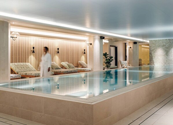 Una piscina interior moderna con sillones de descanso y zona de spa.
