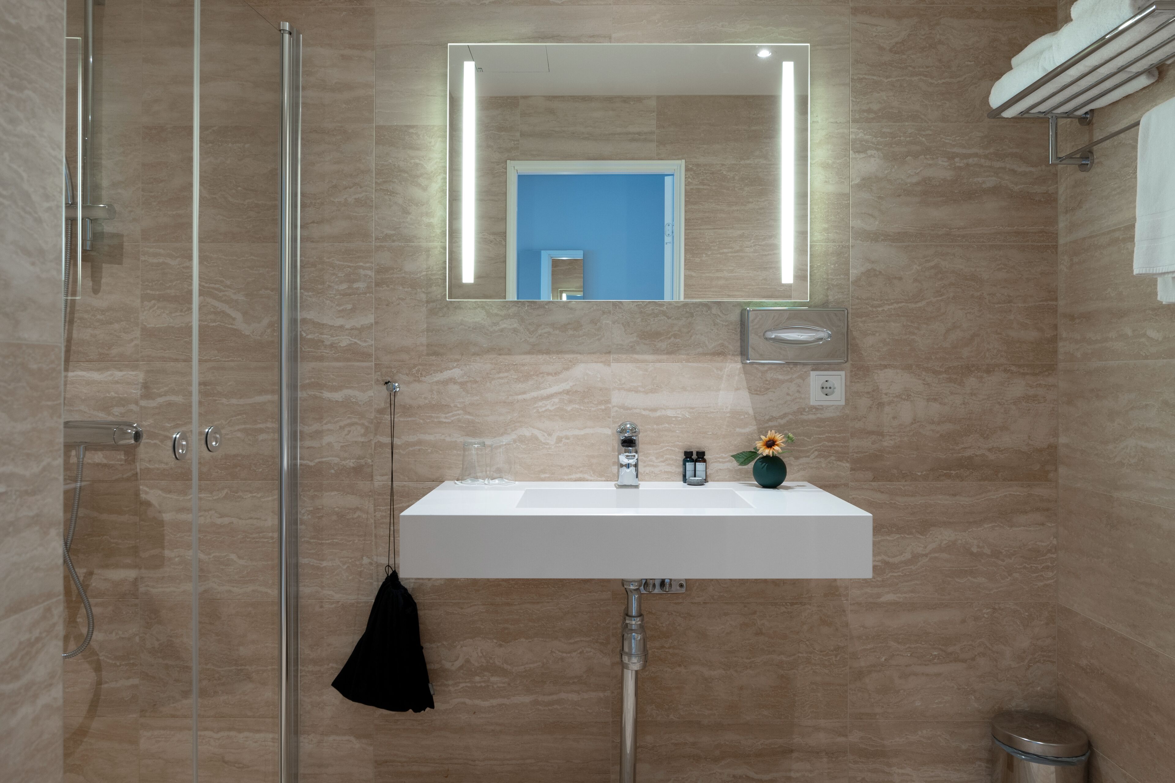 Een moderne badkamer met een douchecabine van glas, een wit wastafelmeubel met een spiegel erboven en een handdoekrek met een handdoek.