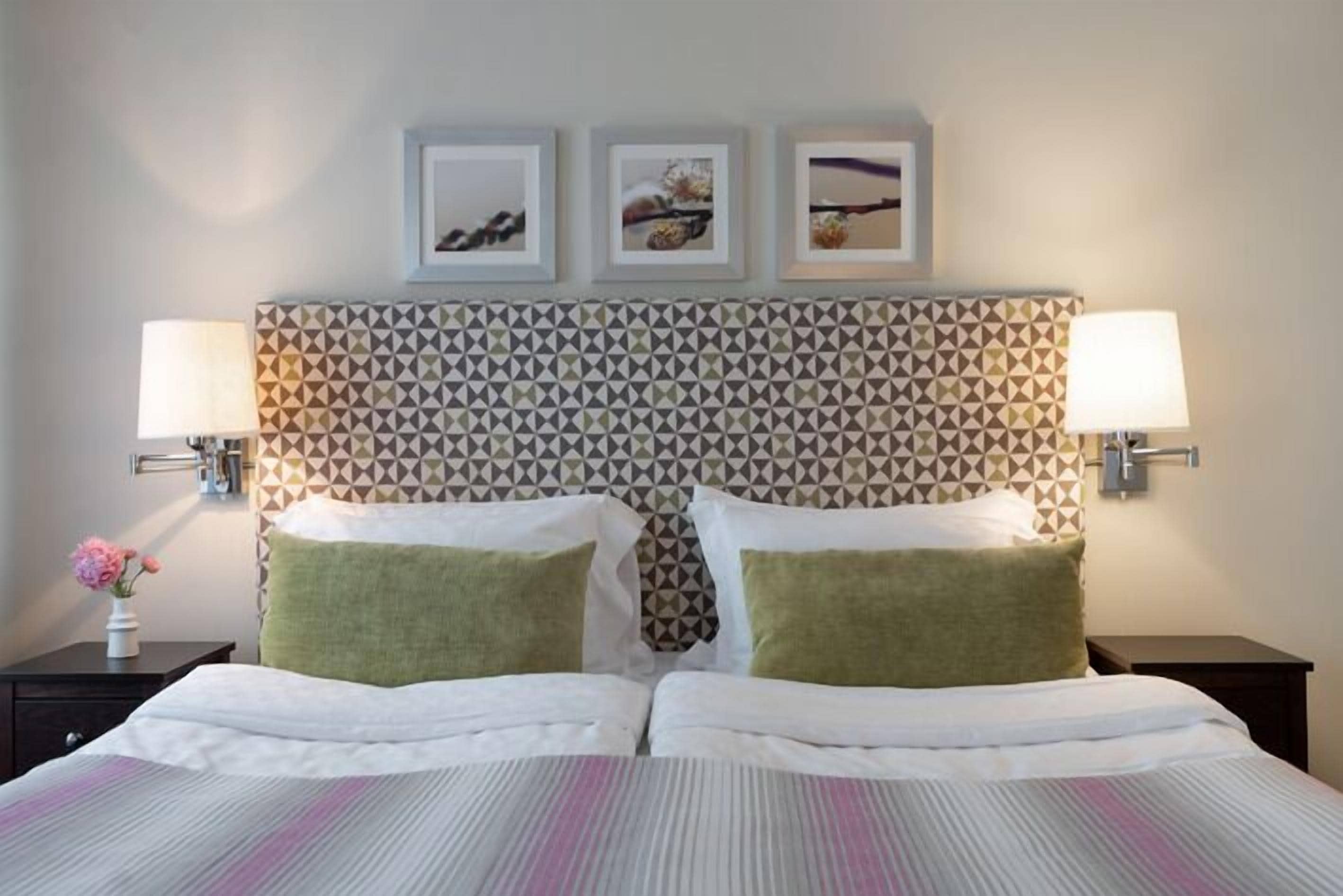 Habitación de hotel con un cabecero estampado, dos camas con almohadas verdes y blancas, y tres cuadros enmarcados en la pared.