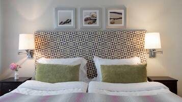 Habitación de hotel con un cabecero estampado, dos camas con almohadas verdes y blancas, y tres cuadros enmarcados en la pared.