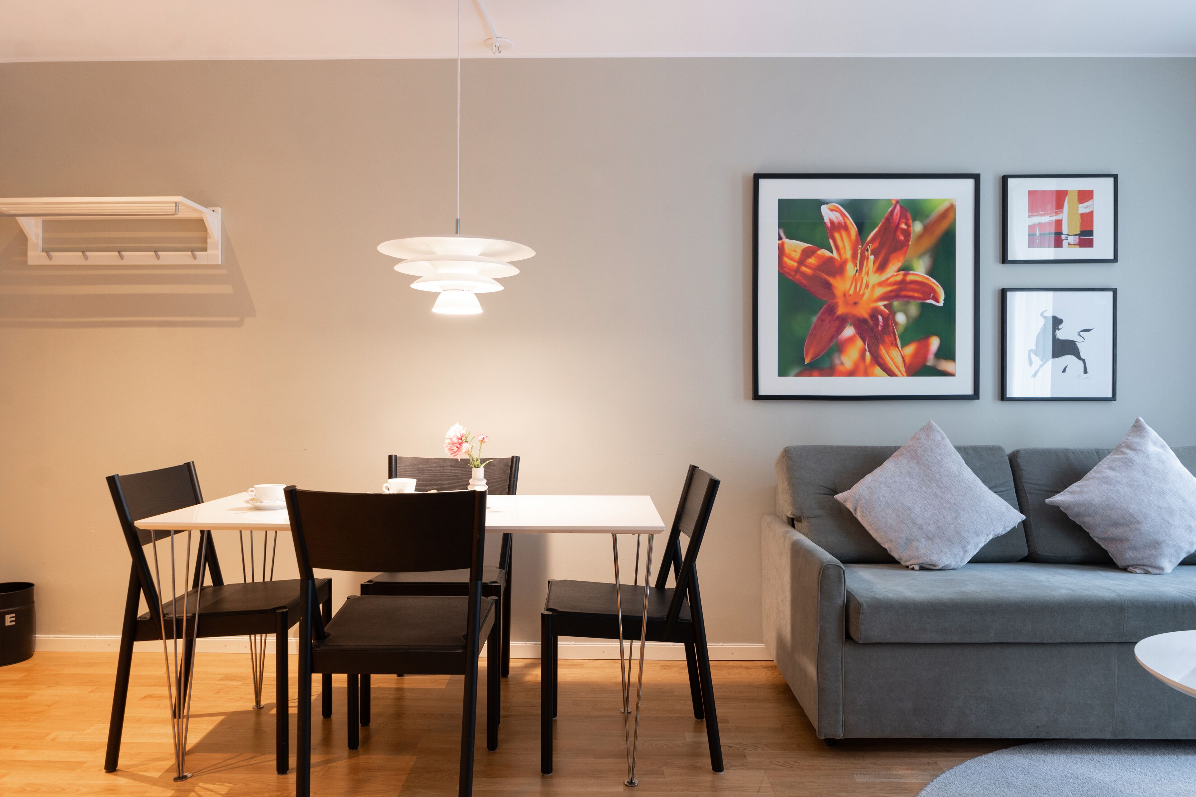 A modern living room with a grey sofa, a dining table with chairs, and a hanging light fixture.