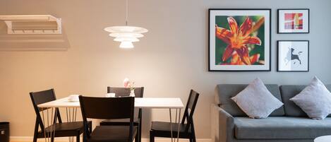 A modern living room with a grey sofa, a dining table with chairs, and a hanging light fixture.