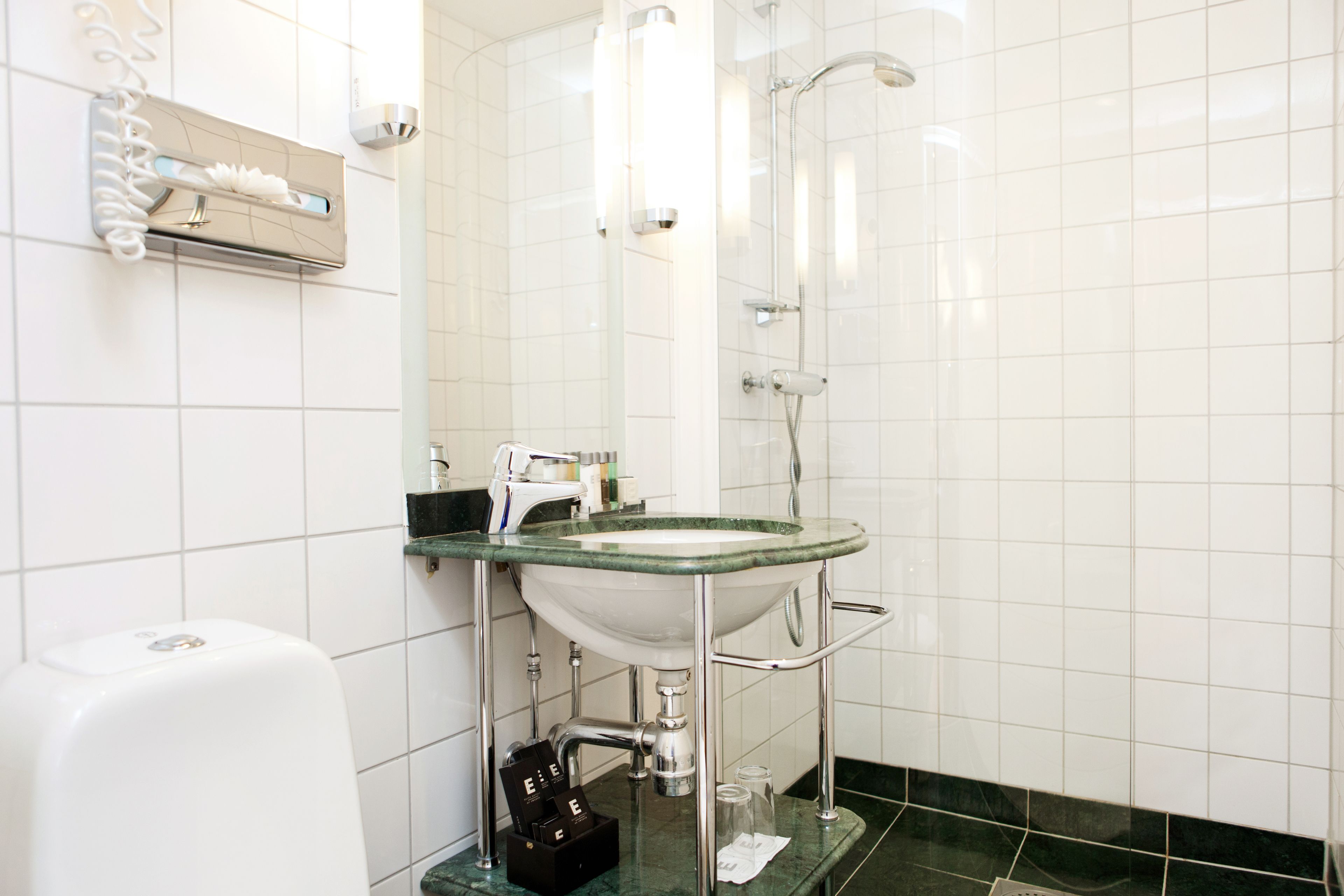 Un baño con lavamanos blanco, cabina de ducha de vidrio y dispensador de jabón.