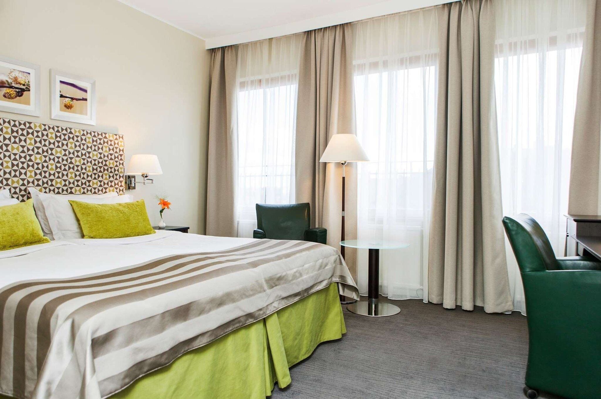Una habitación de hotel con cama, escritorio, silla y lámpara.