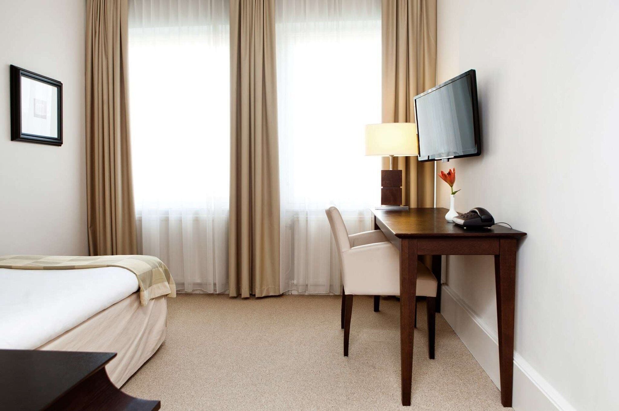 Une chambre d’hôtel avec un lit, un bureau doté d’une lampe, une chaise, un téléviseur et un tableau encadré au mur.
