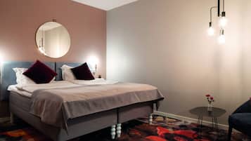 A neatly made bed with a headboard, a round mirror above it, and a small table with a vase of flowers.