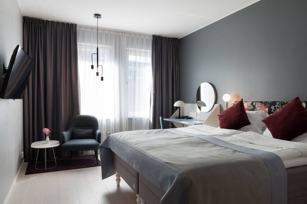 Une chambre d’hôtel moderne équipée d’un lit, d’un bureau, d’une chaise, d’une télévision et d’une fenêtre avec des rideaux.