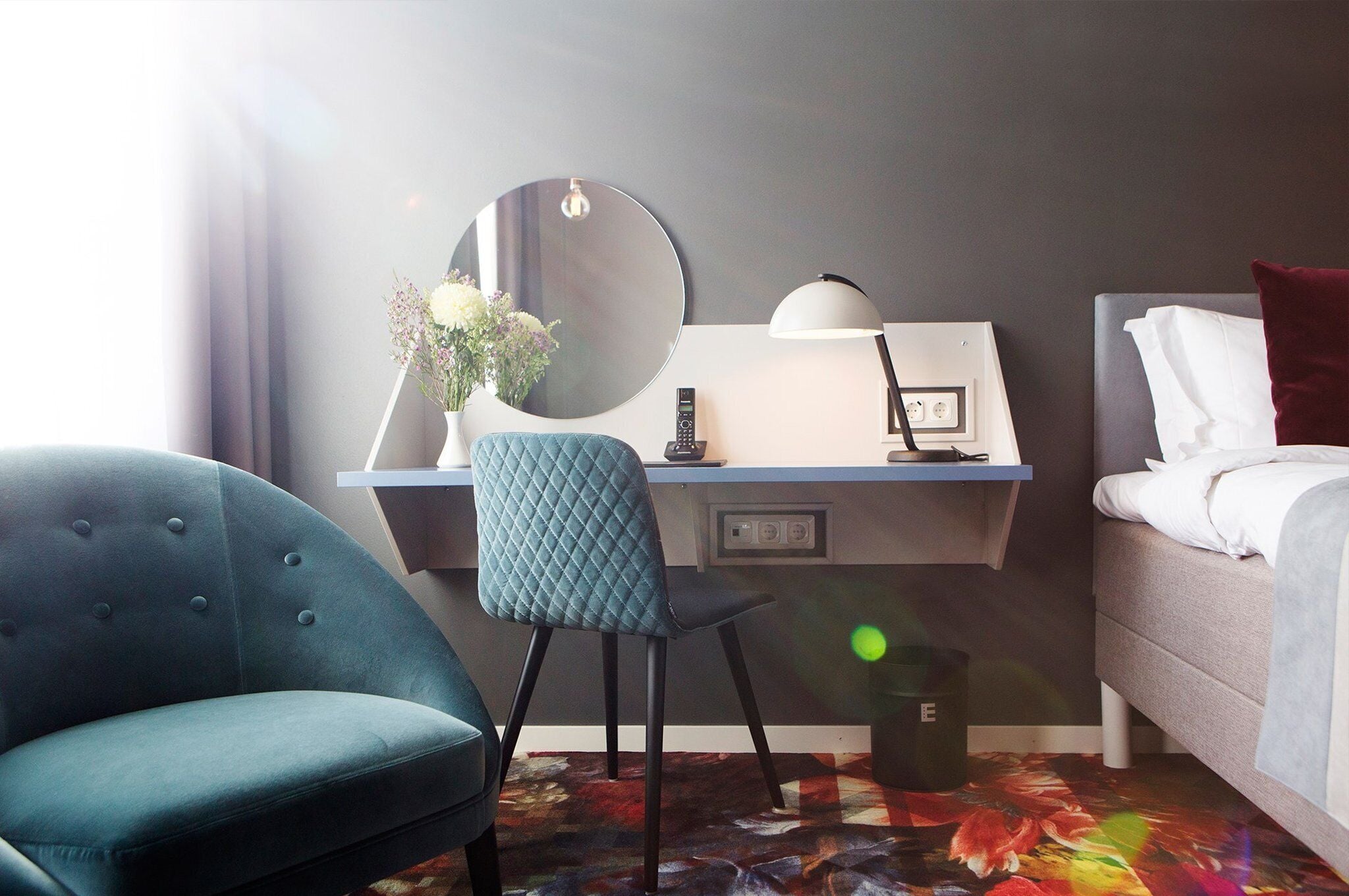 A hotel room with a desk, chair, bed, and a large mirror.