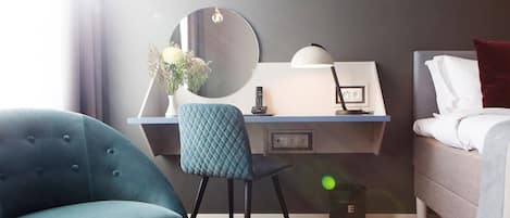 A hotel room with a desk, chair, bed, and a large mirror.