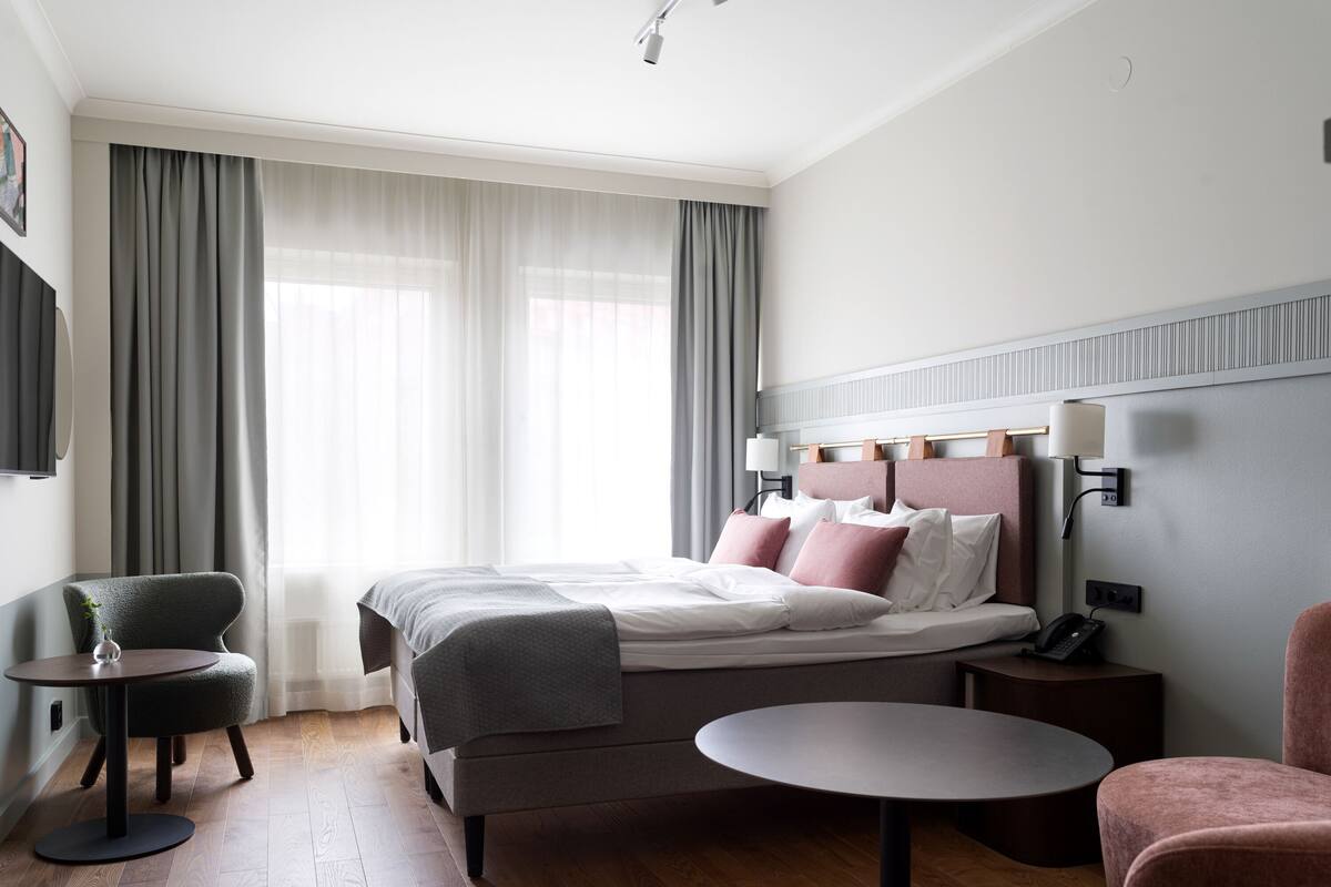 Une chambre d’hôtel moderne avec un lit bien fait, une table ronde, une chaise et une petite table d’appoint.
