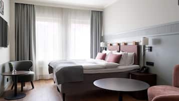 Una habitación de hotel moderna con una cama bien hecha, una mesa redonda, una silla y una mesita auxiliar.