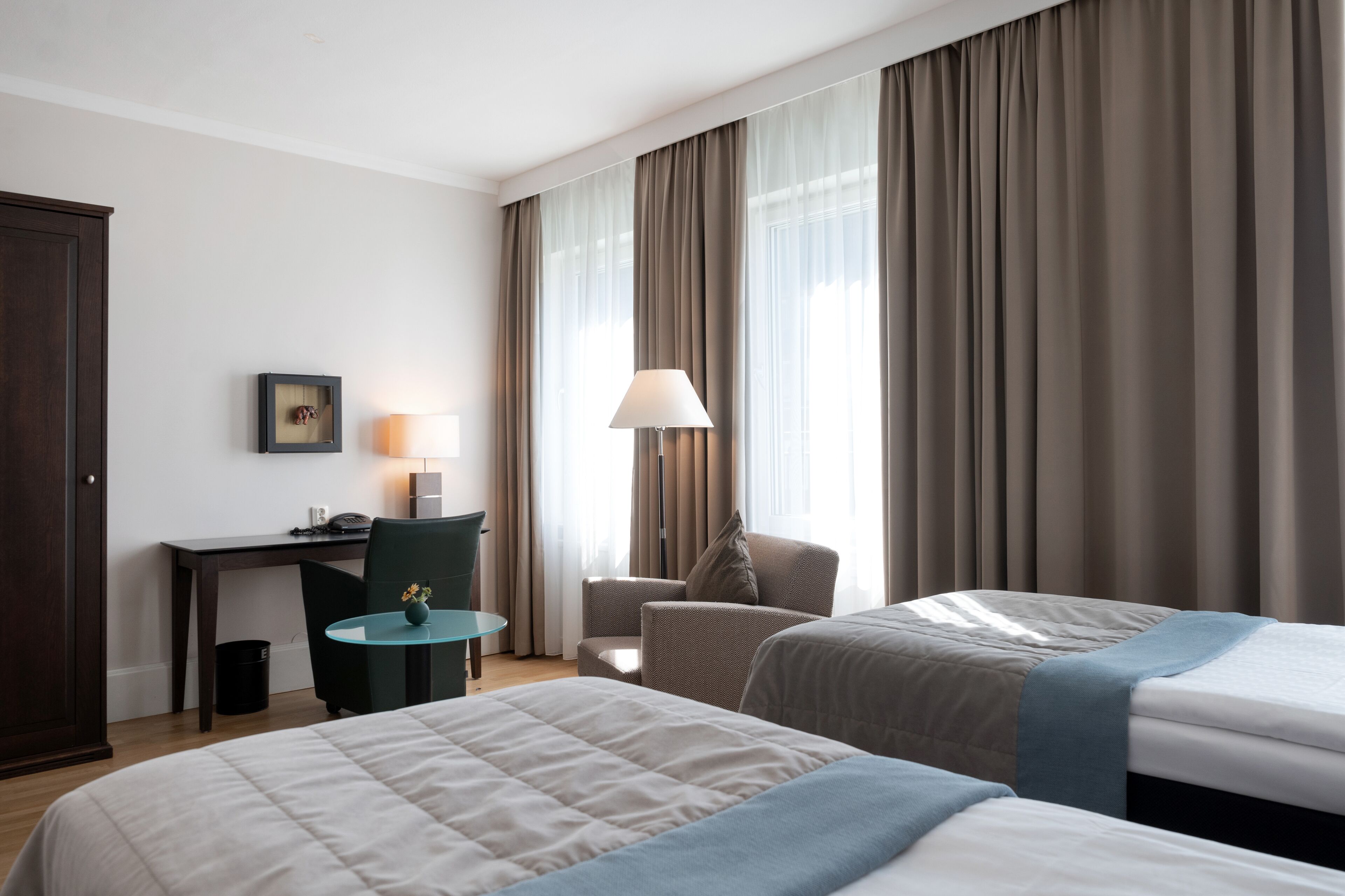 A hotel room with two beds, a desk, a chair, a lamp, and a window with curtains.