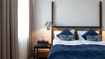 Un letto rifatto con una coperta blu scuro, un comodino con una lampada e un punto luce a parete.