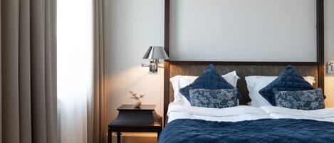 A neatly made bed with a dark blue quilt, a bedside table with a lamp, and a wall-mounted light fixture.