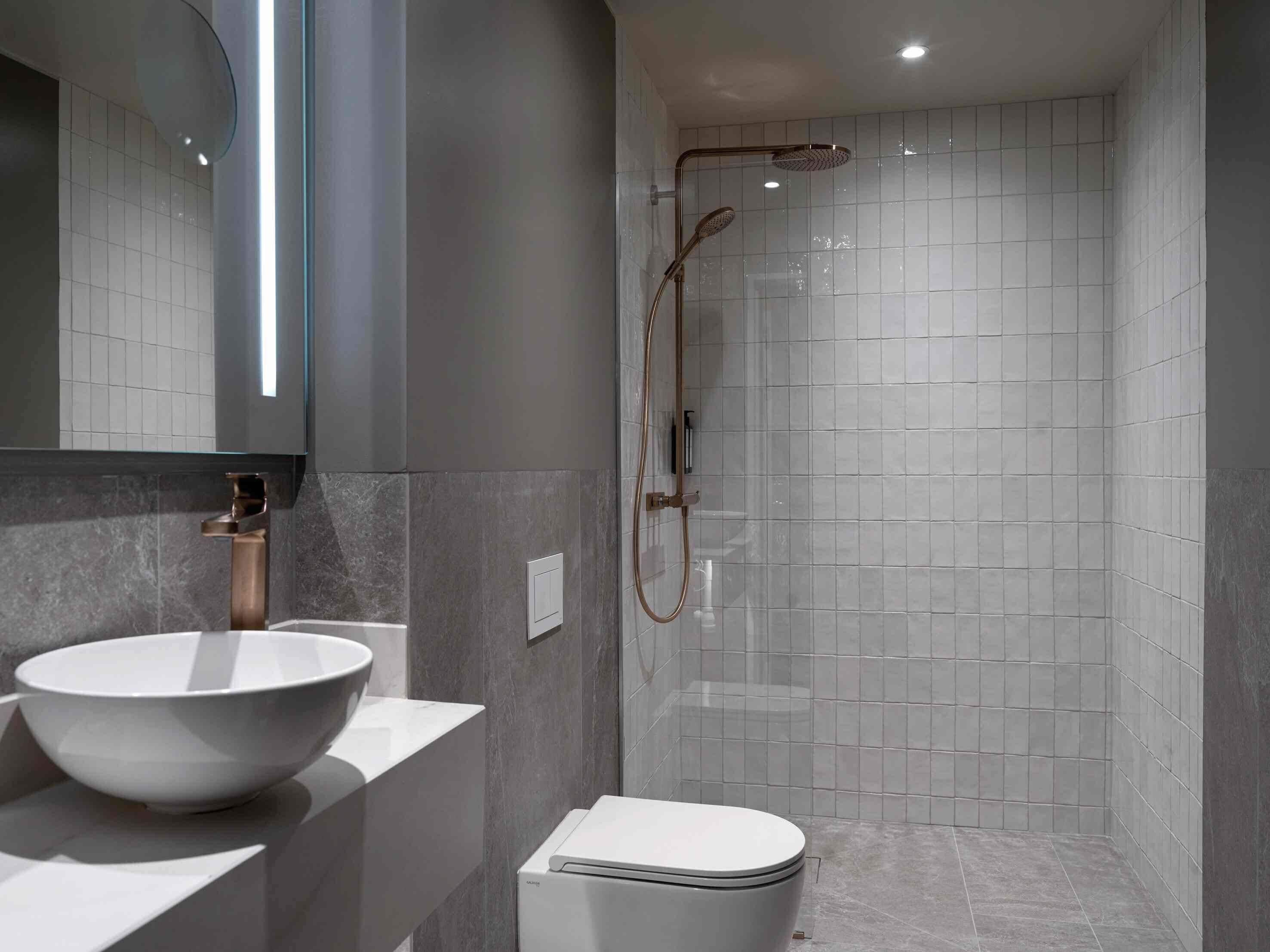 Un baño moderno con un lavamanos blanco de diseño, un inodoro y una ducha a ras de suelo con puerta de cristal.