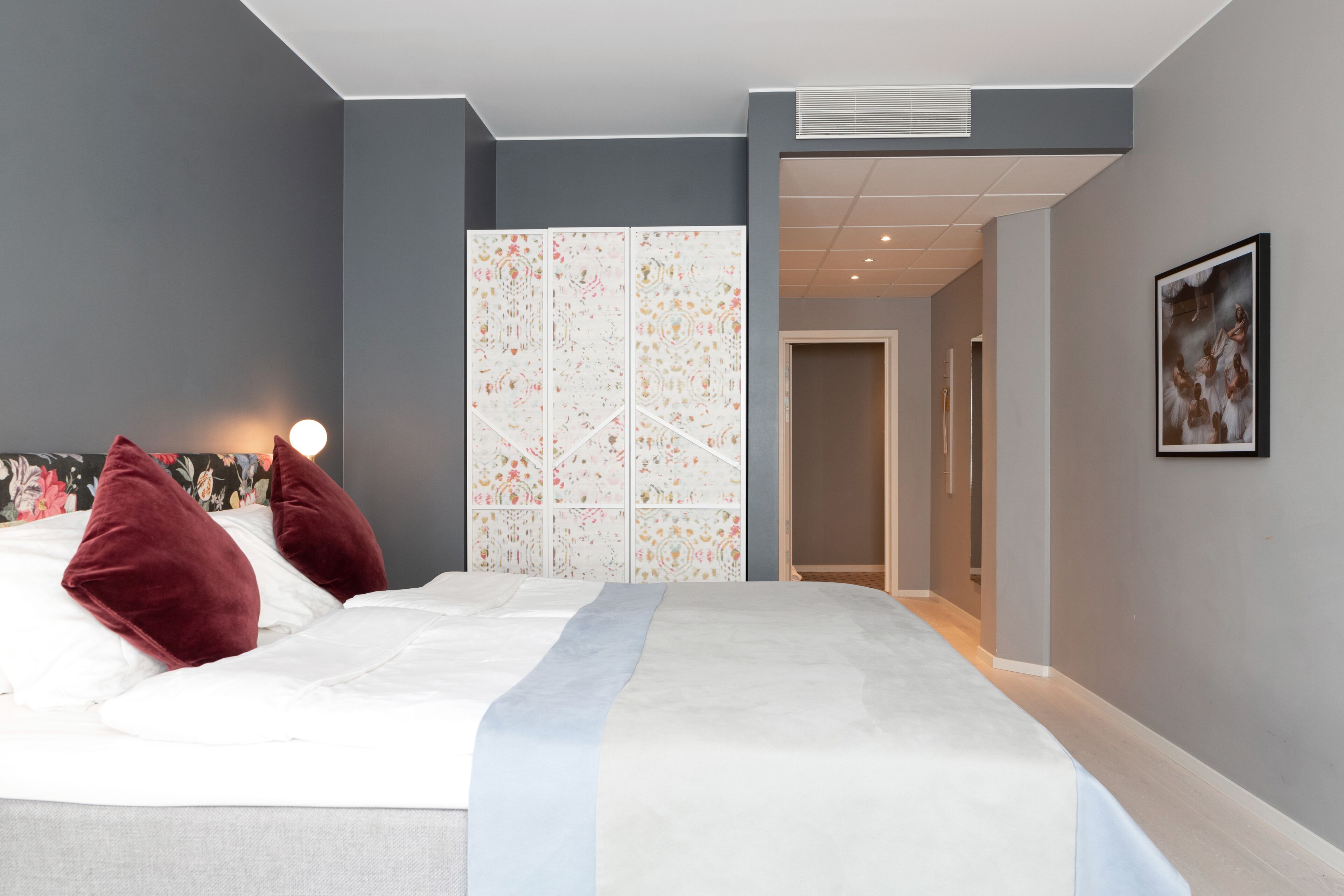 A modern bedroom with a large bed, a decorative wall panel, and a framed picture on the wall.