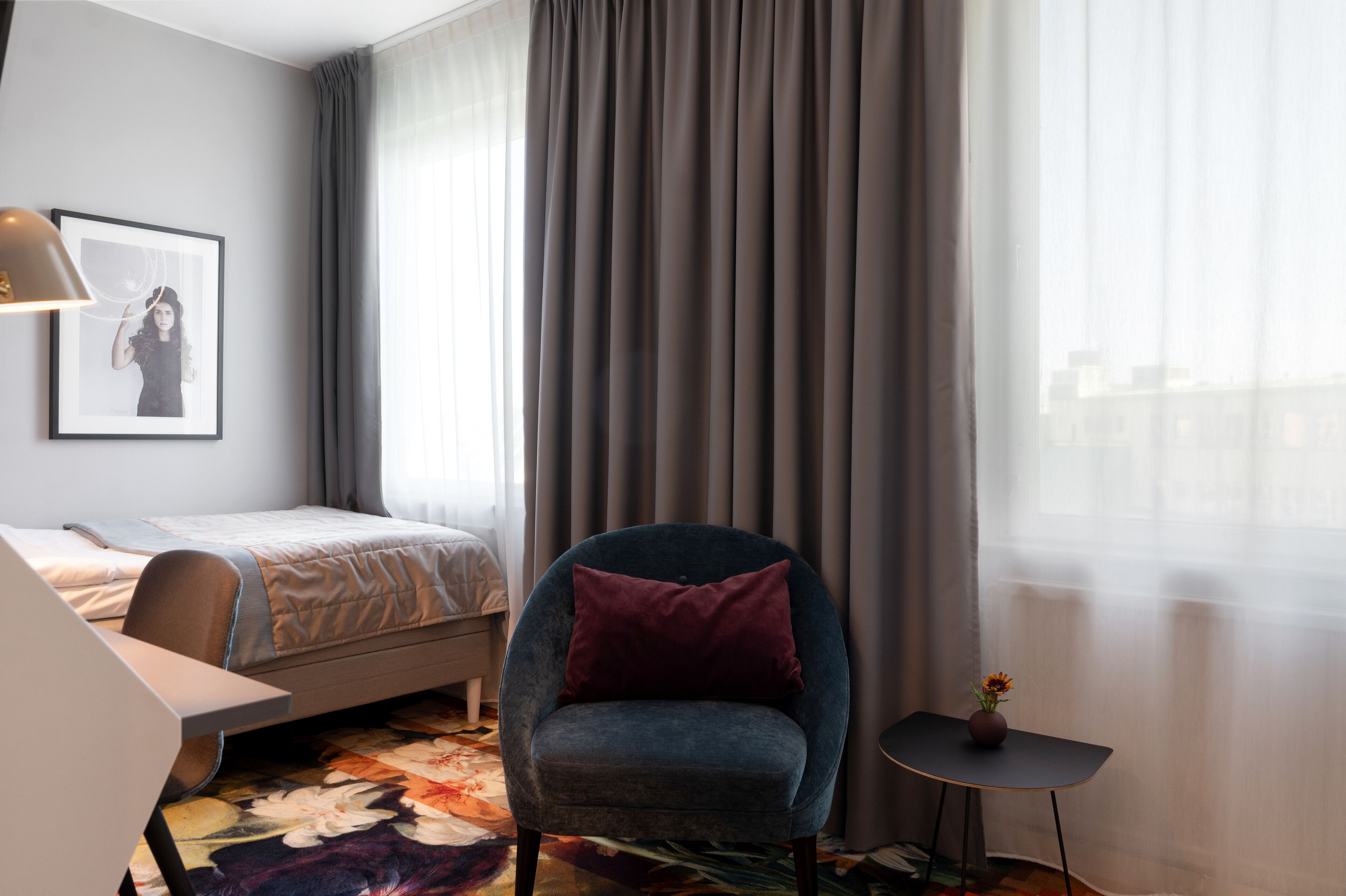 Habitación de hotel con cama, una silla, una mesita y un cuadro en la pared.